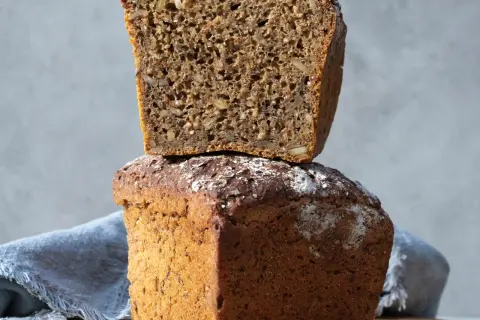 Två limpor, en staplad på den andra. Den övre är uppskuren och visar en rik textur av frön. Perfekt för att baka limpa!