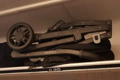 En hopfälld barnvagn, märkt "MINU", ligger som handbagage på en hylla.
