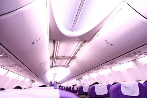 Rad av lila ving flygplan sittplatser med vita nackstöd, belysta av taklampor.