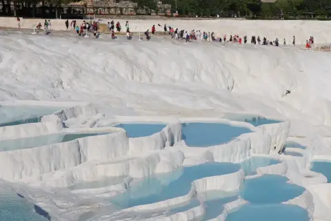 Turister njuter av de turkosa bassängerna vid Pamukkale i Turkiet, ett naturligt underverk av vita kalkstensterrasser.
