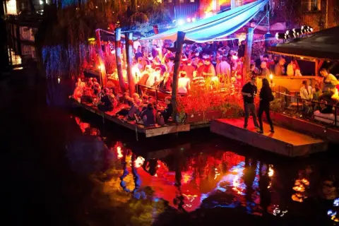 Folk festar på en flytande nattklubb i Berlin. Ljusen reflekteras i vattnet.