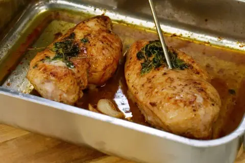 Två saftiga kycklingfiléer i en ugnsform, redo att dras isär till pulled chicken. En termometer mäter temperaturen.
