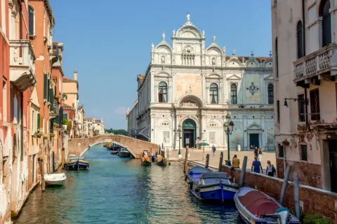 En vacker vy av en del av Venedig med kanaler, broar och historiska byggnader. Båtar ligger förtöjda längs kanalen.