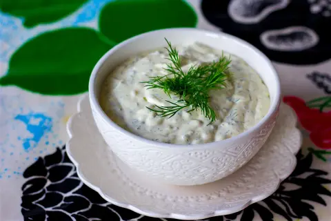 Krämig skolans fisksås med dill, serverad i en vit skål på ett mönstrat underlägg.