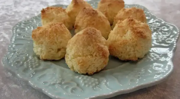 Små, gyllene kokostoppar ligger uppradade på en vacker ljusblå tallrik. Perfekta att baka med detta kokostoppar recept!