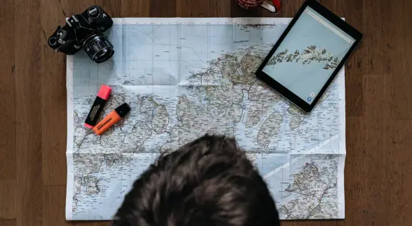Planerar en resa ensam. Karta, kamera, surfplatta och överstrykningspennor ligger redo.