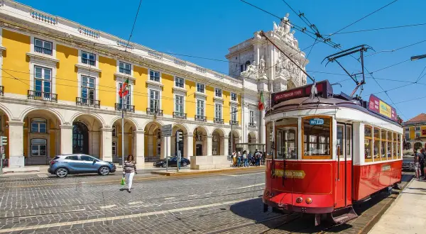 Röd spårvagn i Lissabon, perfekt för en interrail eu-resa. Gula byggnader och en triumfbåge i bakgrunden.