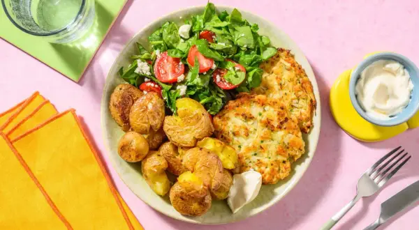 En tallrik med krispiga potatisar, en fräsch sallad med tomat och fetaost, och gyllene fiskkakor. Ett perfekt sallad recept för en lätt lunch.