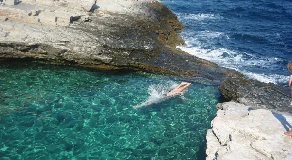 En person simmar i turkost vatten vid en klippig kust på Thassos, Grekland.