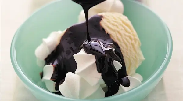 En skål med vaniljglass och visp täcks av glansig chokladsås. Ett perfekt chokladsås recept för en lyxig dessert.