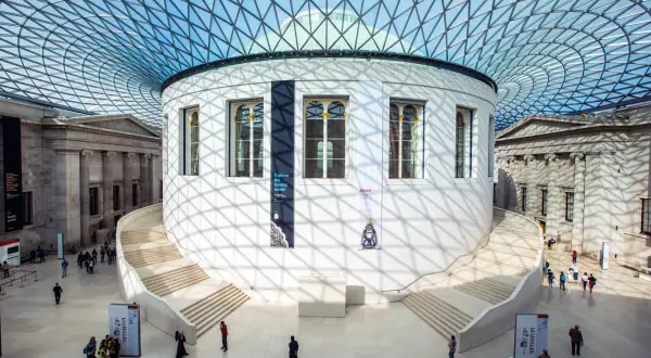 Storslagen arkitektur i London, med en imponerande glasstruktur som tak. En rund byggnad med trappor leder uppåt, omgiven av klassiska pelare. Här finns konst och historia att utforska.