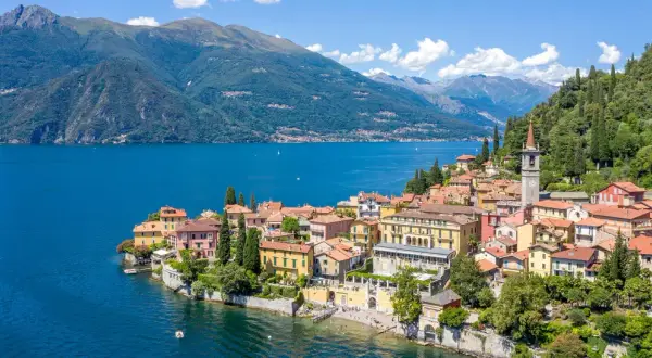 Färgstark by vid en blå sjö i norra Italien, med gröna berg i bakgrunden.