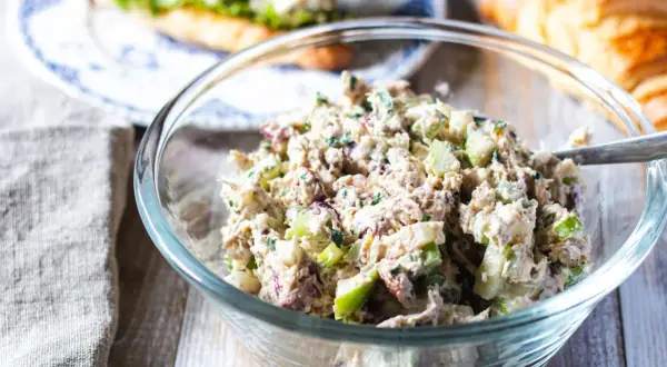 En skål med krämig kycklingsallad, perfekt för ett kycklingsallad recept. I bakgrunden syns en croissant och en smörgås.
