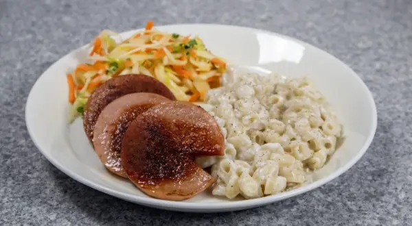 En tallrik med stuvade makaroner, stekt falukorv och en fräsch sallad. En klassisk svensk måltid.