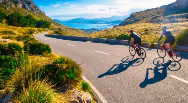 Två cyklister njuter av en solig dag med att cykla på Mallorca, med en vacker vy över havet och bergen.