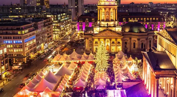 En livlig julmarknad i Berlin med tält, en stor julgran och upplysta byggnader i skymningen.