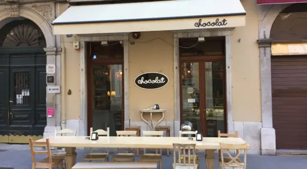 Uteservering vid ett chokladcafé i Trieste, Italien. Långt bord med stolar och bänkar framför butiken.
