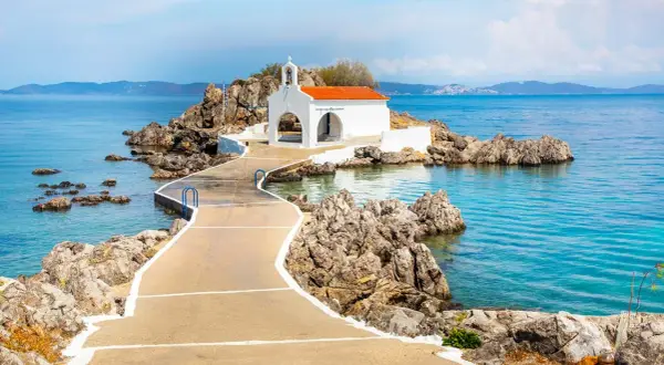 En vit kyrka med orange tak på en klippig ö, nås via en gångväg. Vackert vid Skiathos, Grekland.
