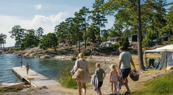 Familj på väg mot vattnet för en härlig sommarsemester med barn. Sol, bad och campingliv vid en svensk sjö.