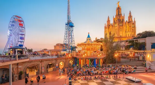 Tivoli i solnedgången med pariserhjul, karusell och en imponerande kyrka. Perfekt för Barcelona aktiviteter med familjen.
