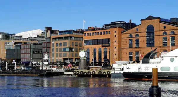 En del av Oslo med moderna byggnader, en gammal tegelbyggnad med ett stort klocktorn vid vattnet och båtar.