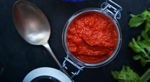 En burk med kryddig mojo rojo bredvid en sked och färska örter.