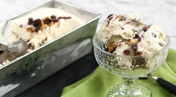 En skål med krämig nicecream banan, toppad med chokladbitar och nötter. Bredvid står en form med mer glass.