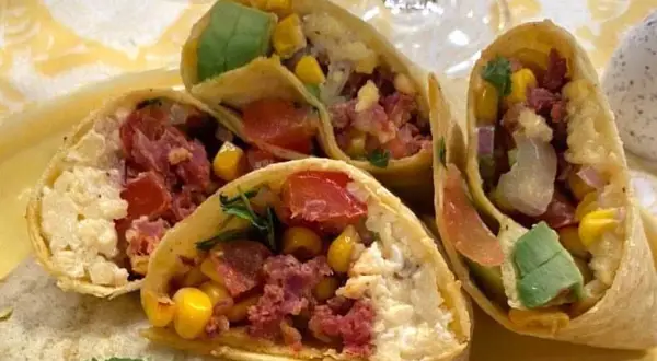 En närbild på en frukost burrito fylld med majs, tomat, avokado och kött.