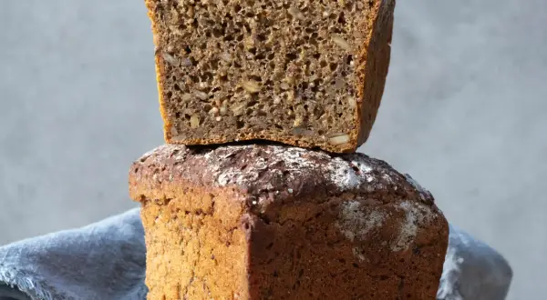 Två limpor, en staplad på den andra. Den övre är uppskuren och visar en rik textur av frön. Perfekt för att baka limpa!