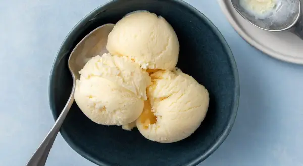Tre skopor krämig vaniljglass i en mörkblå skål med en sked. Perfekt för ett enkelt gelato recept.