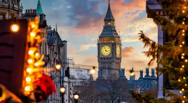 Big Ben lyser upp en magisk london julmarknad. Julgranar med ljus och vackra byggnader skapar en festlig stämning i solnedgången.