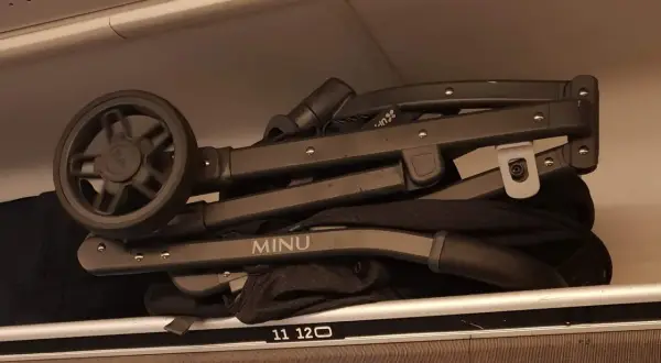 En hopfälld barnvagn, märkt "MINU", ligger som handbagage på en hylla.