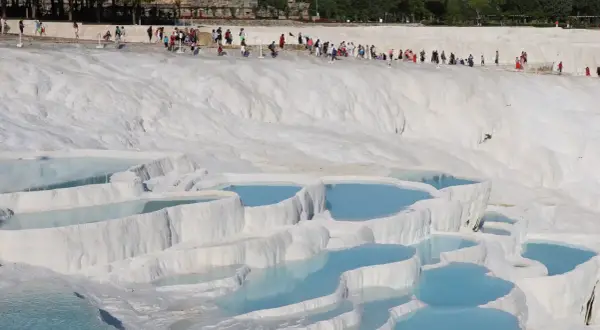 Turister njuter av de turkosa bassängerna vid Pamukkale i Turkiet, ett naturligt underverk av vita kalkstensterrasser.