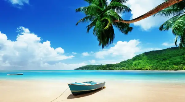 En blå båt på en sandstrand med palmer och turkost vatten. En dröm om Maldiverna eller Mauritius.
