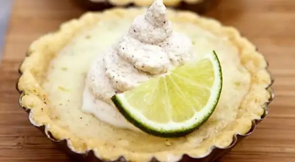 En liten key lime pie med en klick grädde och en limeklyfta.