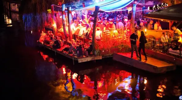 Folk festar på en flytande nattklubb i Berlin. Ljusen reflekteras i vattnet.