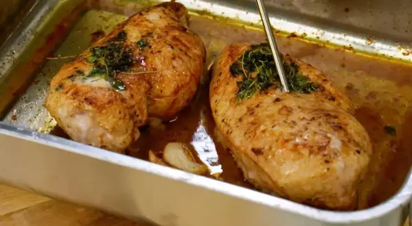 Två saftiga kycklingfiléer i en ugnsform, redo att dras isär till pulled chicken. En termometer mäter temperaturen.