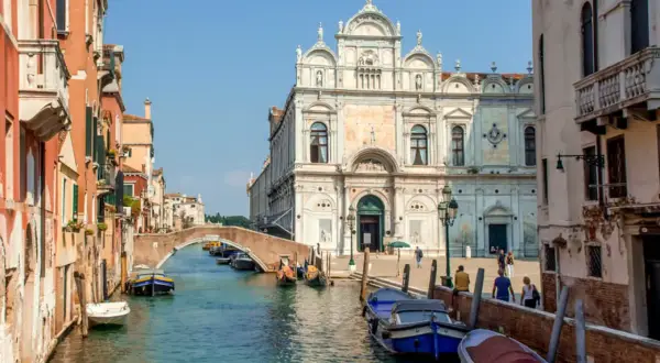 En vacker vy av en del av Venedig med kanaler, broar och historiska byggnader. Båtar ligger förtöjda längs kanalen.