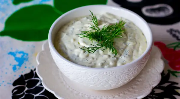 Krämig skolans fisksås med dill, serverad i en vit skål på ett mönstrat underlägg.