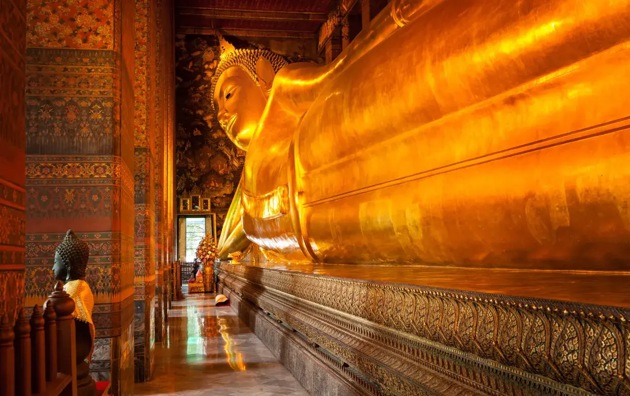 Stor gyllene liggande Buddha i ett tempel i Bangkok. En mindre Buddha-staty står till vänster.