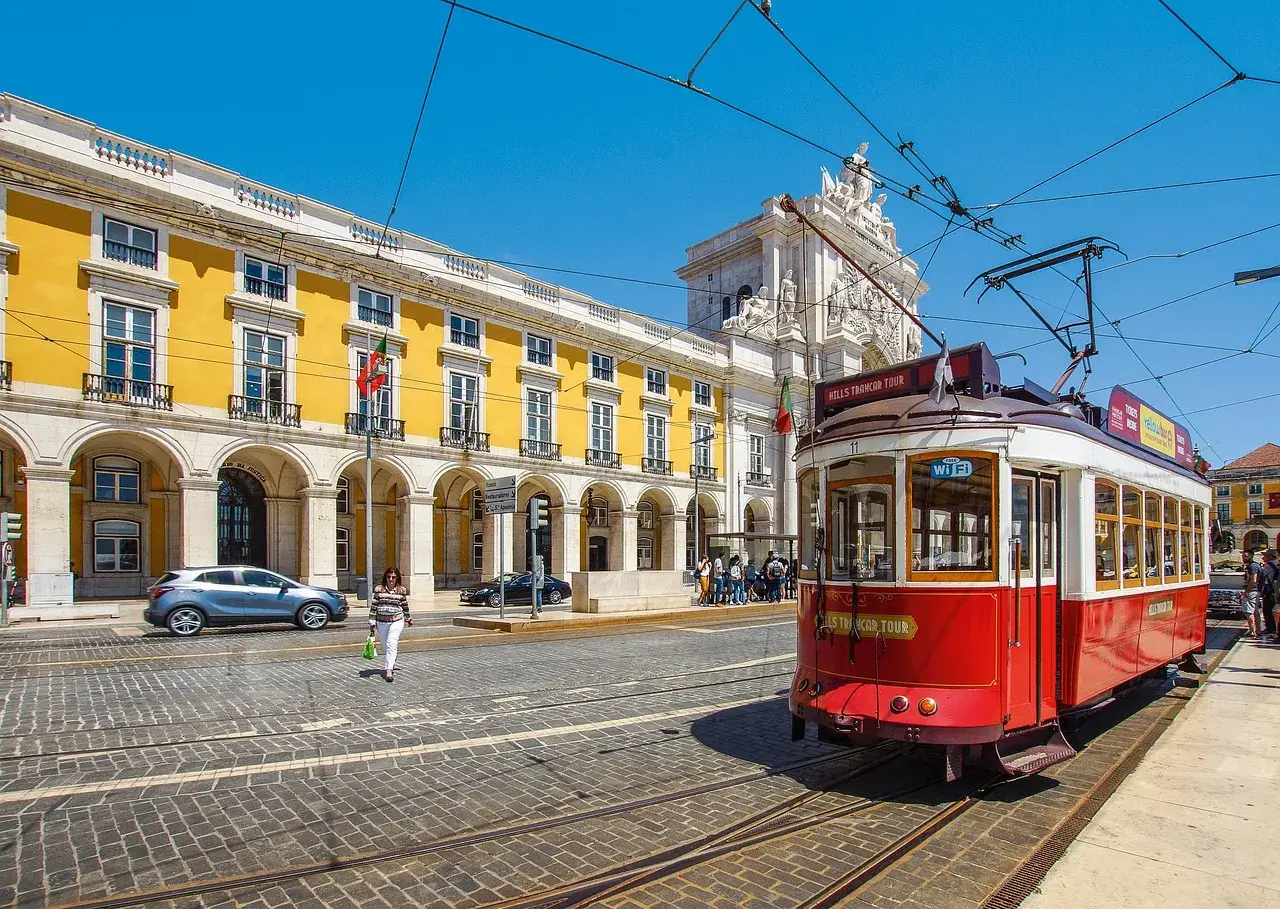 Röd spårvagn i Lissabon, perfekt för en interrail eu-resa. Gula byggnader och en triumfbåge i bakgrunden.