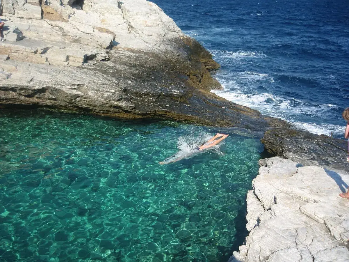 En person simmar i turkost vatten vid en klippig kust på Thassos, Grekland.