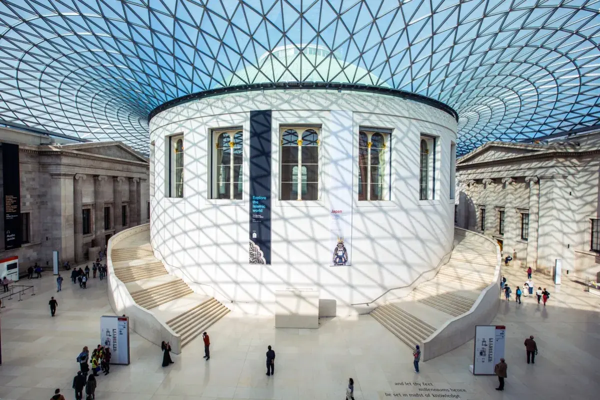 Storslagen arkitektur i London, med en imponerande glasstruktur som tak. En rund byggnad med trappor leder uppåt, omgiven av klassiska pelare. Här finns konst och historia att utforska.