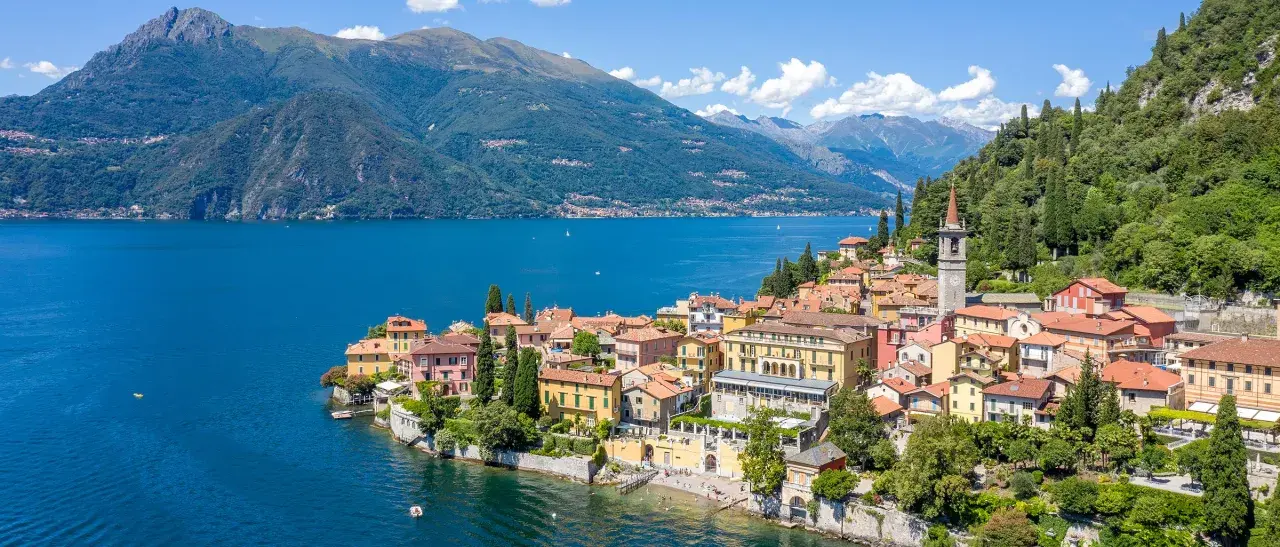 Färgstark by vid en blå sjö i norra Italien, med gröna berg i bakgrunden.