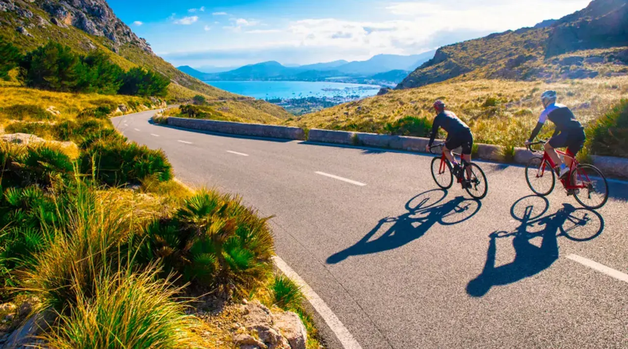 Två cyklister njuter av en solig dag med att cykla på Mallorca, med en vacker vy över havet och bergen.