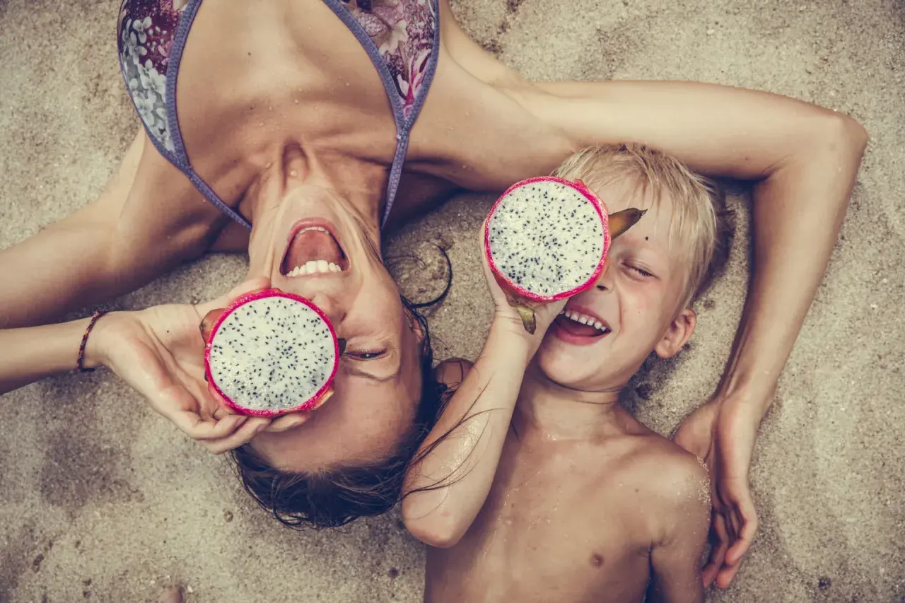 Glad mamma och barn på stranden i Thailand med drakfrukt.