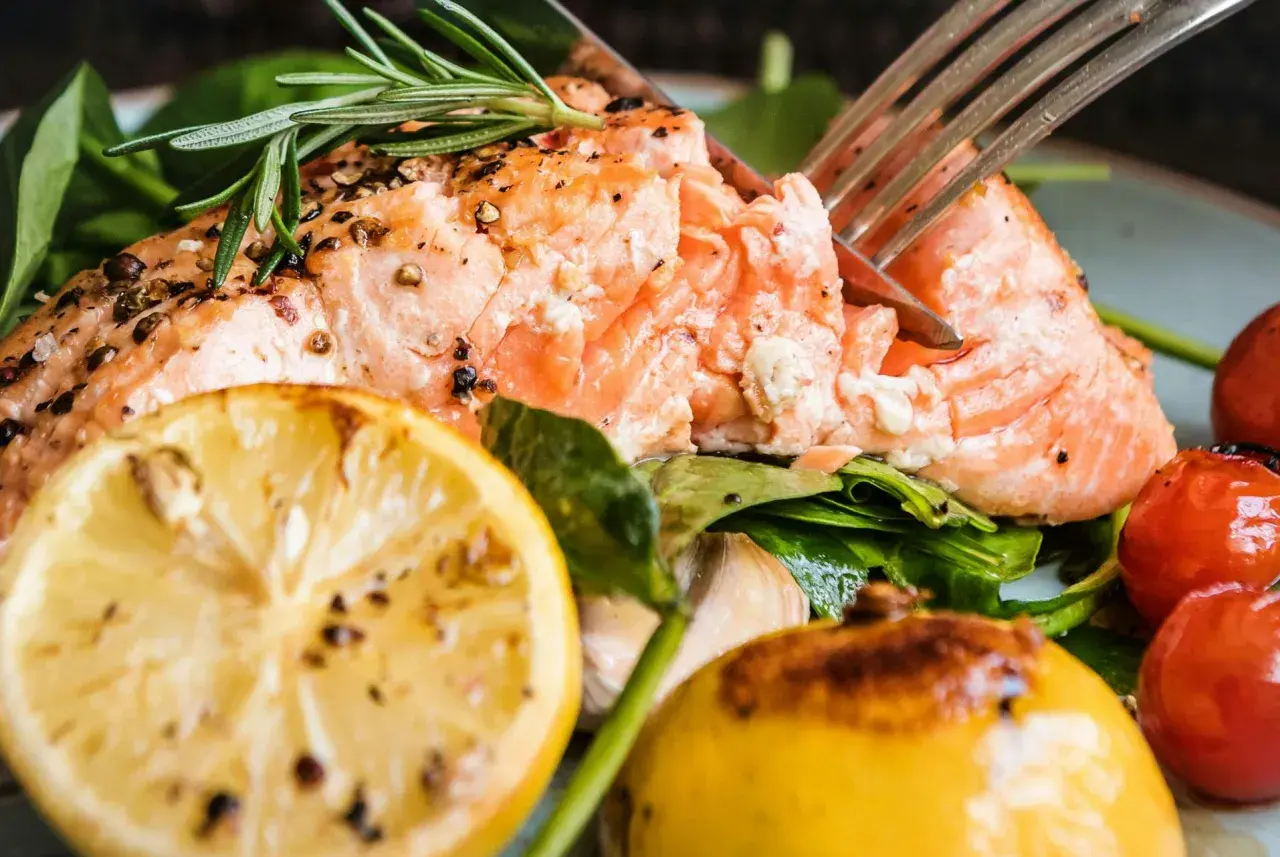 En saftig bit lax i ugn, perfekt kryddad med peppar och rosmarin, serverad med citronklyftor och körsbärstomater.