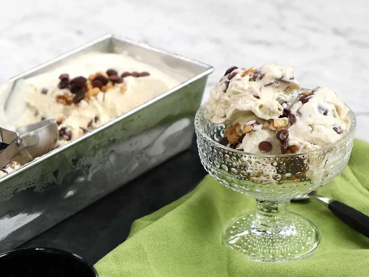 En skål med krämig nicecream banan, toppad med chokladbitar och nötter. Bredvid står en form med mer glass.