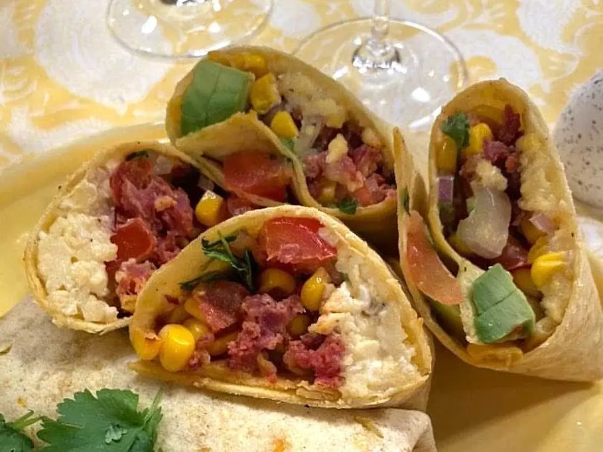 En närbild på en frukost burrito fylld med majs, tomat, avokado och kött.