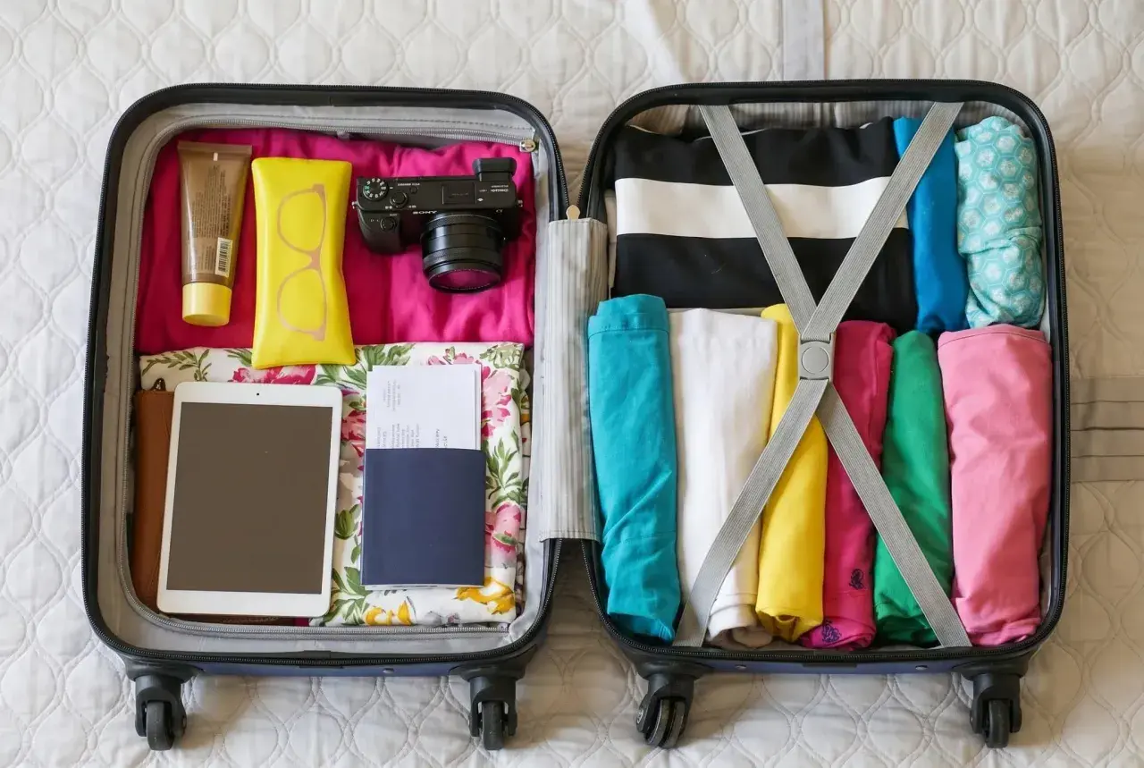 Packad resväska med kläder i glada färger, kamera, solkräm, glasögonfodral, surfplatta och pass. Perfekt för mått handbagage.